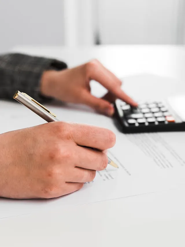 A hand signing a form beside a calculator